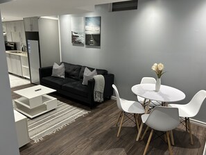 Ein modernes Wohnzimmer mit einer schwarzen Couch, weißen Sesseln, einem kleinen weißen Tisch und einem Esstisch mit einer Blumenvase.