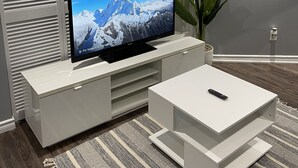 A modern living room with a flat-screen TV on a white entertainment unit, a white coffee table, and a striped rug. - Cozy basement apartment in Brampton  (Brampton)