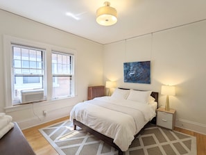 Un dormitorio con cama, lámparas de noche, un radiador y una ventana con persianas.
