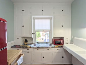 Cocina compacta con armarios blancos, un refrigerador rojo, microondas y ventana con vista al exterior.