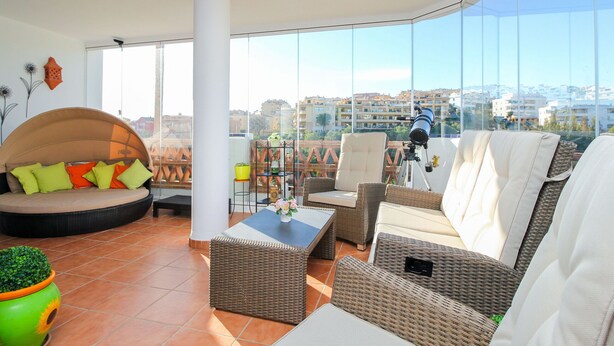 A spacious balcony with wicker furniture, a round seating area, and a large window offering a city view. - Amazing place with large terrace and BBQ (Mijas Costa)