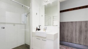 A modern bathroom with a glass shower enclosure, a white vanity with a mirror, and a wooden accent wall. - Apres - Dinner Plain (Dinner Plain)