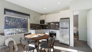 A modern kitchen with white cabinets, stainless steel appliances, and a dining area with a wooden table and chairs. - Apres - Dinner Plain (Dinner Plain)