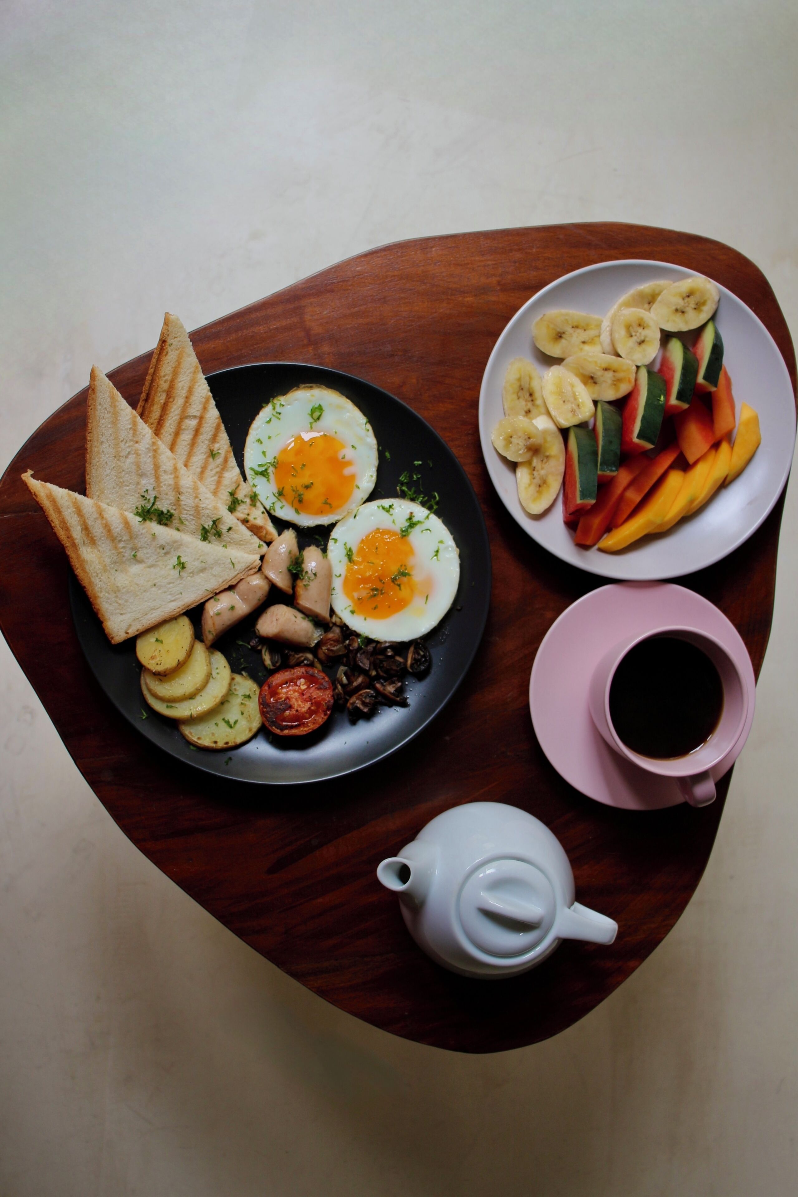 A breakfast plate with toast, eggs, and vegetables, a cup of coffee, and a teapot on a wooden table.