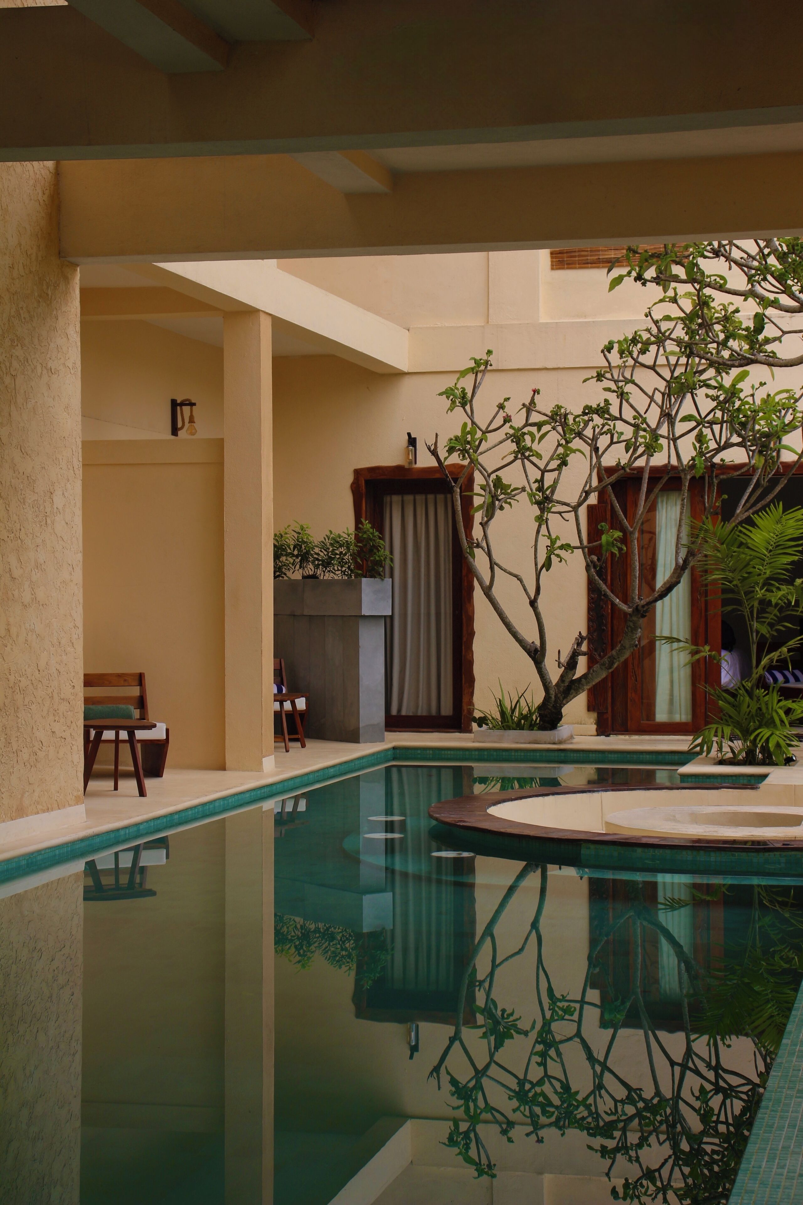 Un área de piscina con superficie de agua cristalina, rodeada de paredes color beige y mobiliario de madera.