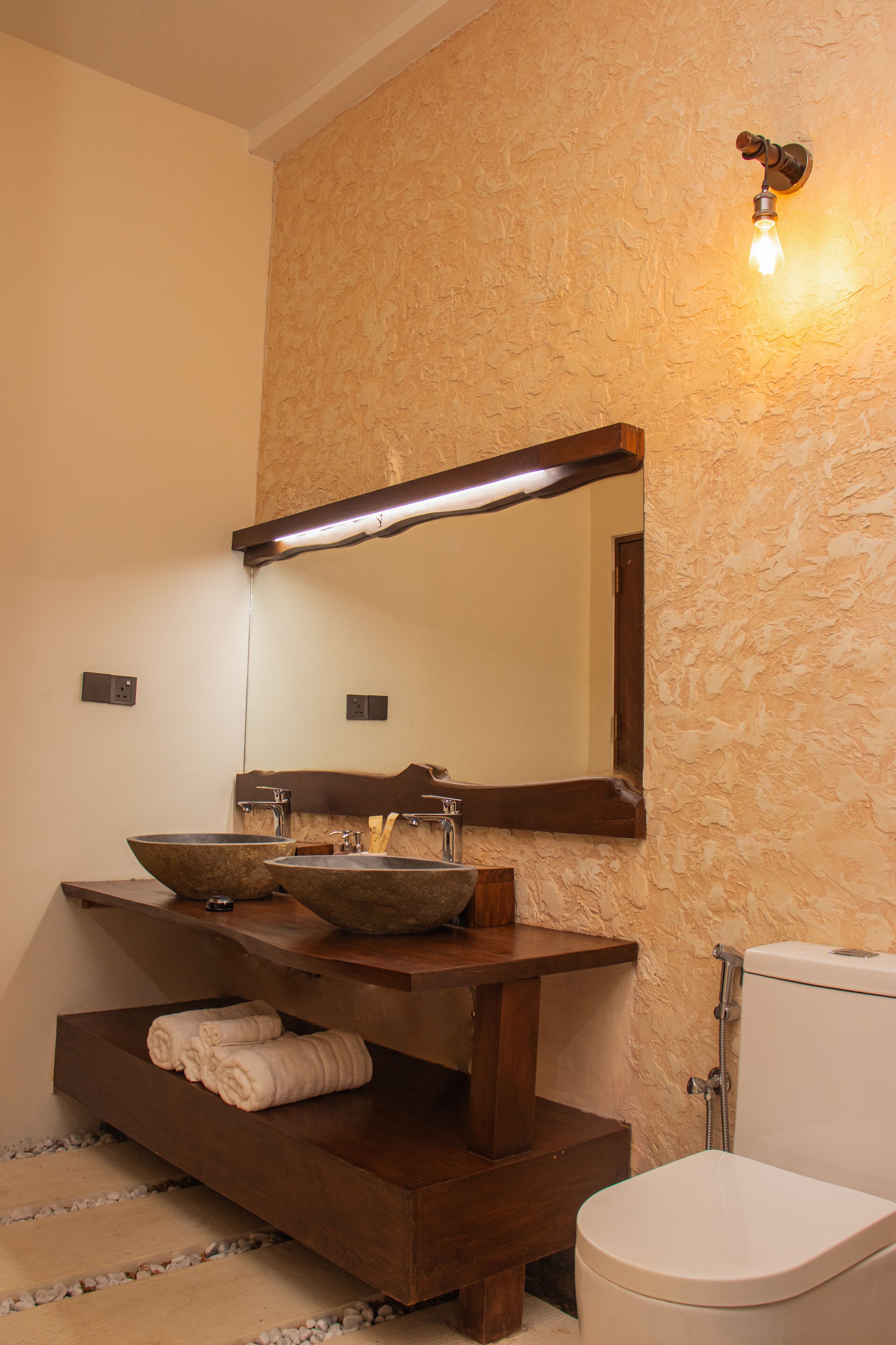 Un baño con un tocador de madera, dos lavamanos, un espejo grande y un inodoro.