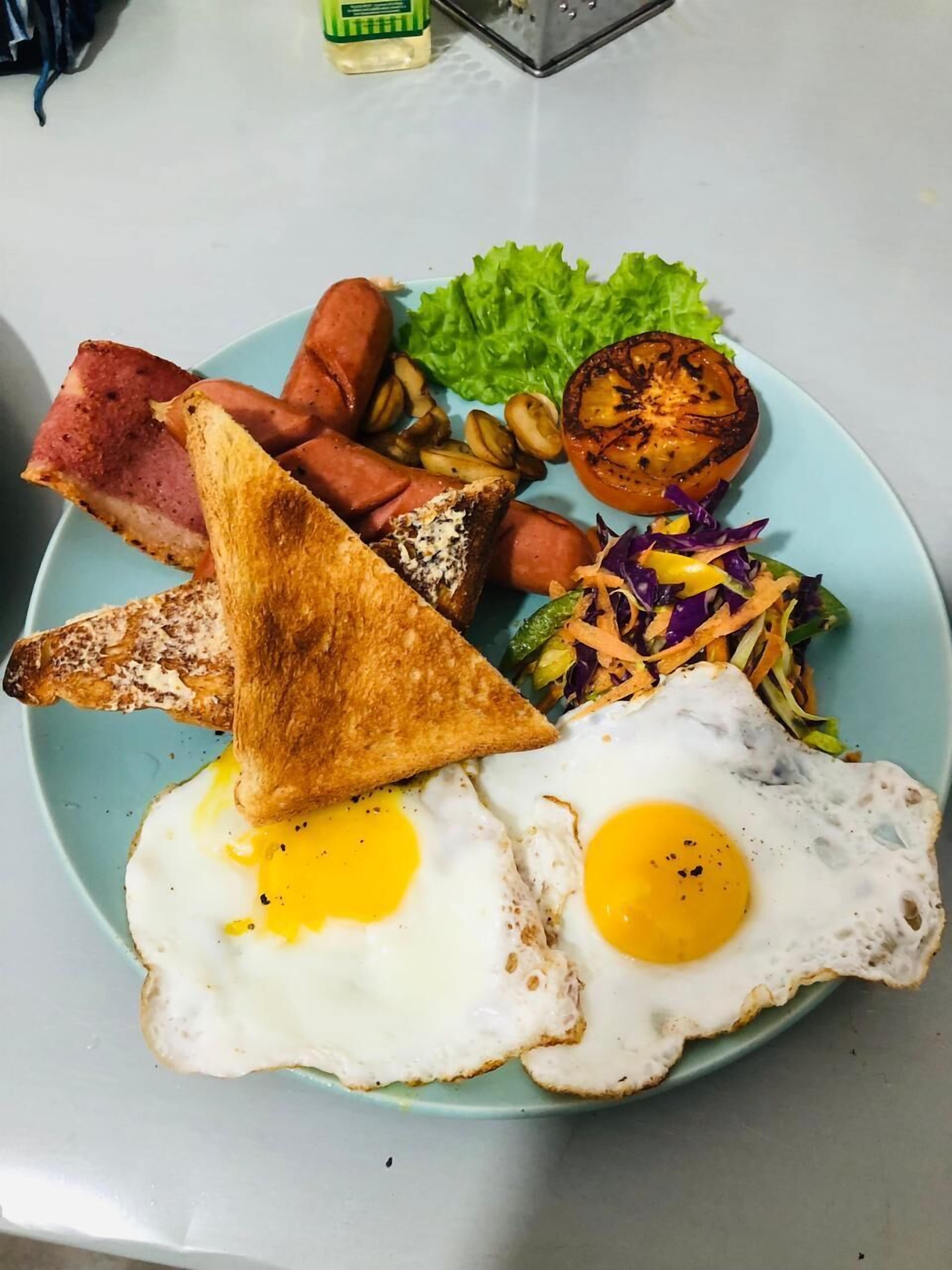 A plate with two fried eggs, toast, bacon, sausages, roasted potatoes, a grilled tomato, and a side salad.