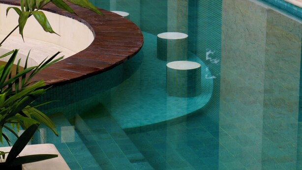 Piscina interior moderna com água cristalina, deck de madeira e um vaso com planta.