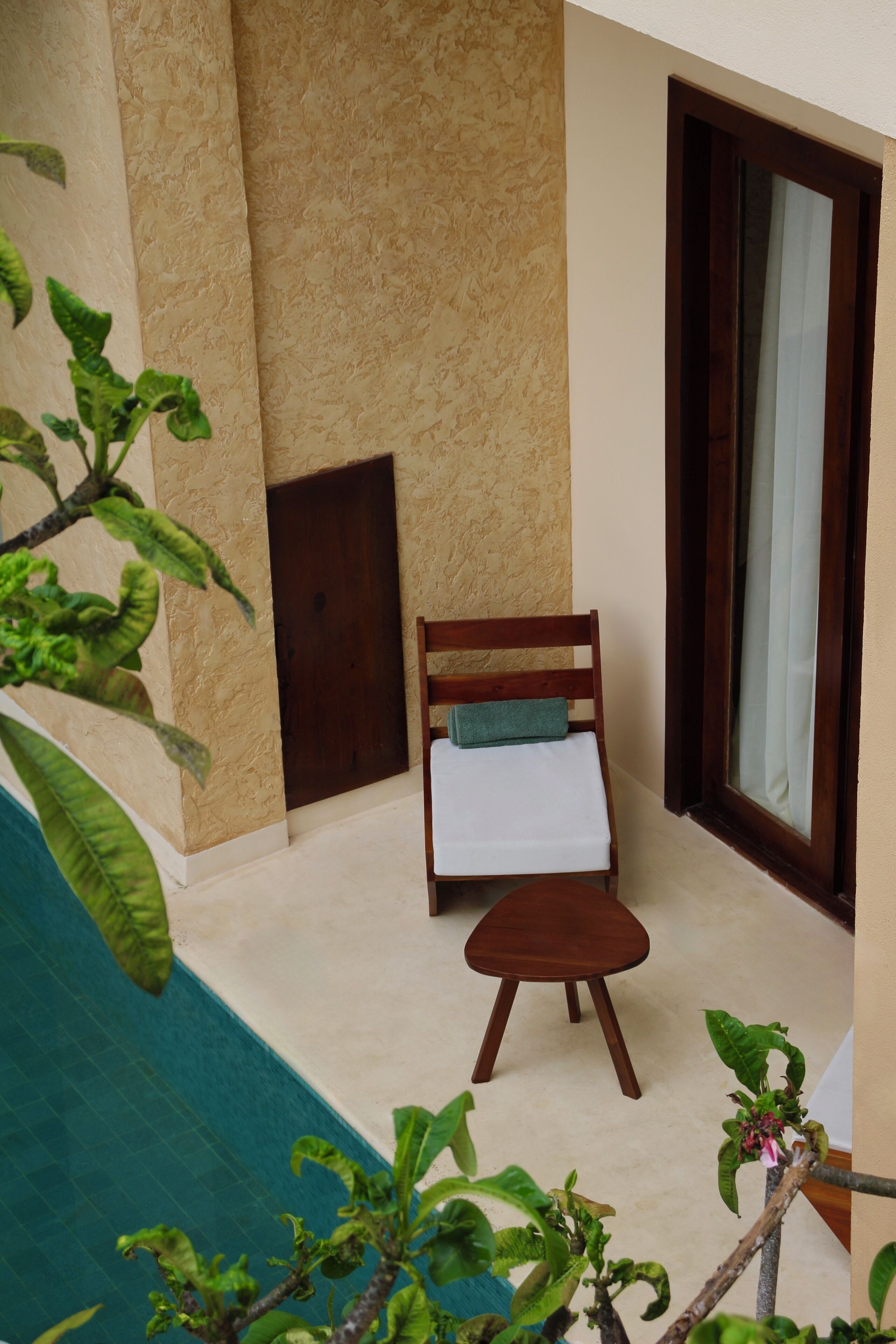 Une petite pièce agréable et chaleureuse, avec une chaise en bois et une petite table, une fenêtre avec des rideaux et une vue sur une piscine.