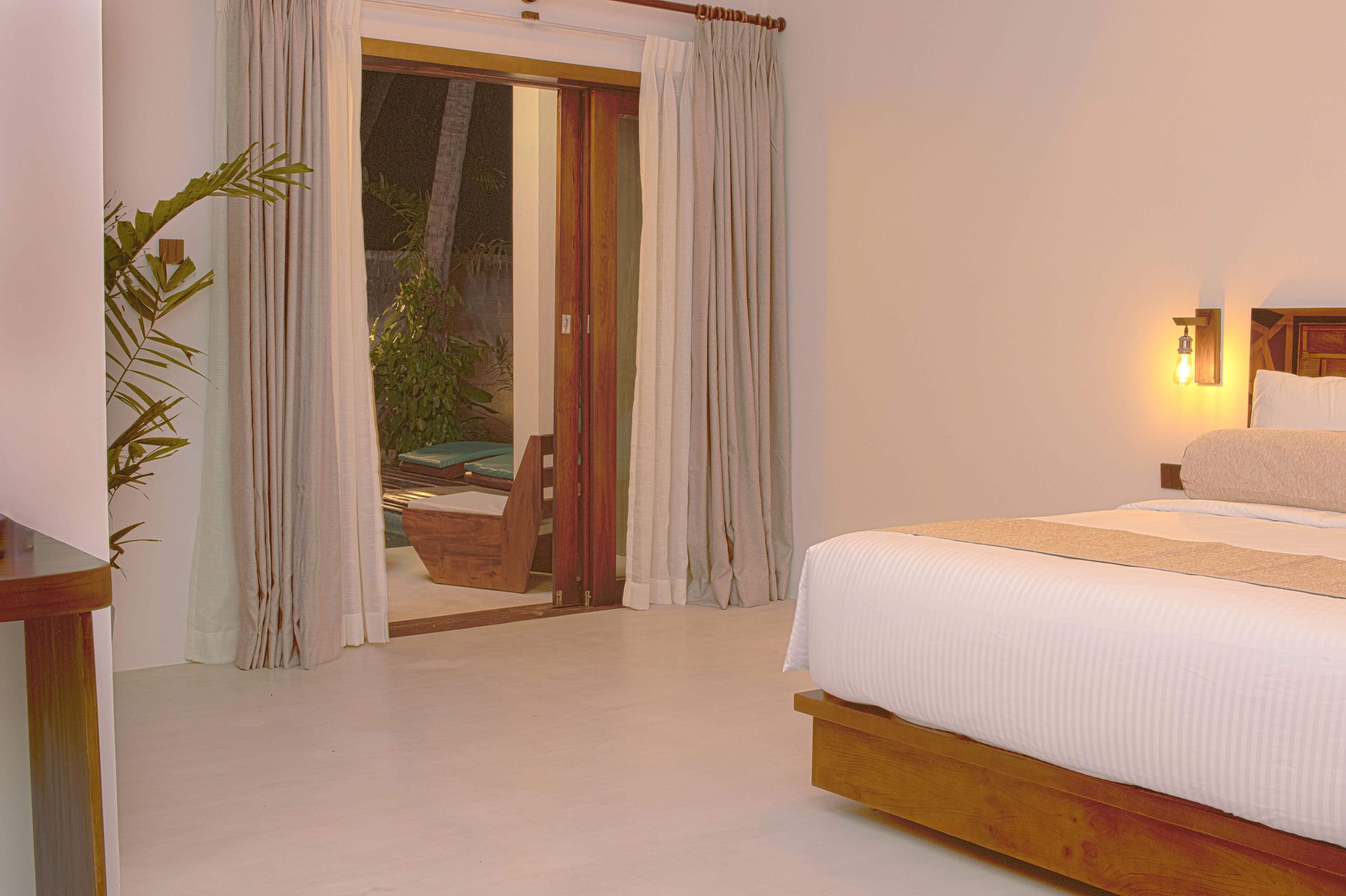 A bedroom with a large bed, a wooden headboard, a nightstand, and a sliding glass door leading to an outdoor area.