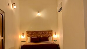 Um corredor estreito que leva a uma cama com cabeceira de madeira e duas luzes fixadas na parede.