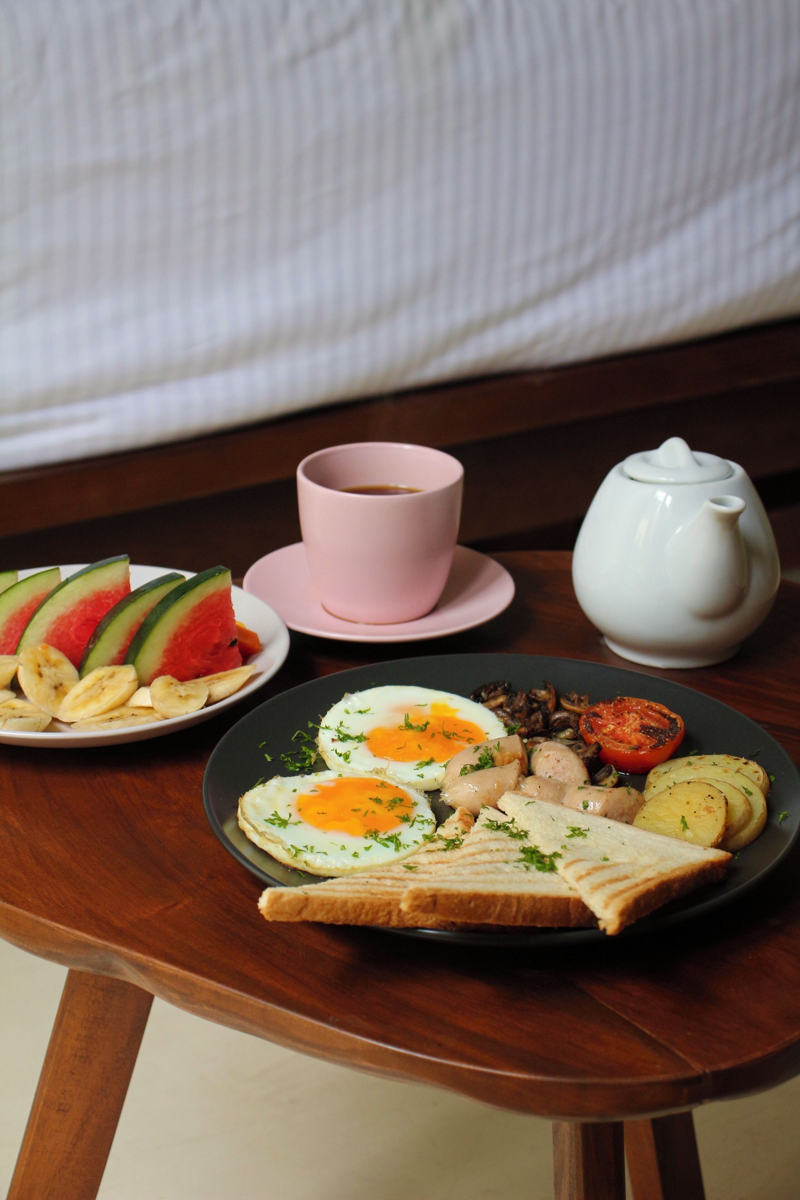A breakfast table with a plate of food, a pink cup, and a white teapot.