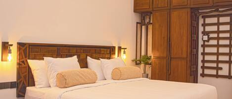 Una cama bien hecha con sábanas blancas y dos almohadas color beige, cabecera de madera y un aire acondicionado montado en la pared.