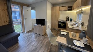 Een moderne kitchenette met een televisie, een eettafel met borden en een bank in een lichte kamer met houten vloeren en een schuifdeur van glas.