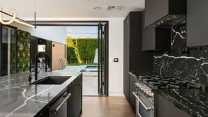Une cuisine moderne dotée d’un plan de travail en marbre noir, d’appareils électroménagers en acier inoxydable et offrant une vue sur un jardin.