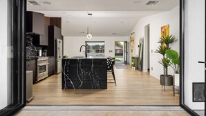 Une cuisine moderne avec un îlot en marbre, un coin repas avec une chaise noire et une vue sur l’extérieur.