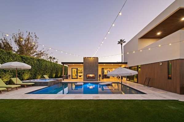 A modern outdoor pool area with lounge chairs, string lights, and a well-maintained lawn.