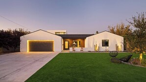 Une maison moderne avec un garage, une pelouse bien entretenue et une terrasse avec des chaises.