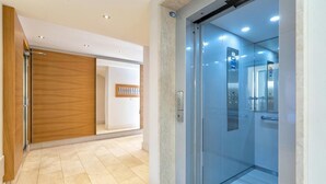 A modern elevator with glass doors, a wooden panel wall, and a tiled floor. - Bilocale Vista Mare Giorgio, Alghero, Italy (Alghero)