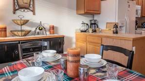 Un comedor con mantel escocés, un centro de mesa con vela y una cocina al fondo.