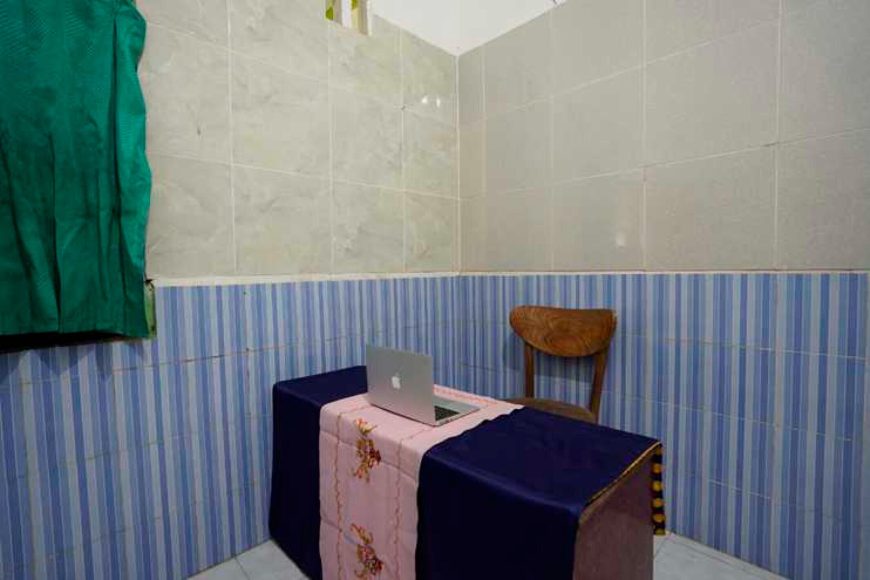 Una habitación pequeña con un muro de azulejos, una silla de madera, una mesa con una computadora portátil y un muro a rayas.