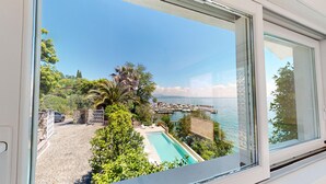 Ein Pool mit Blick auf eine Marina und Boote, umgeben von üppiger Vegetation und einer Steinmauer.