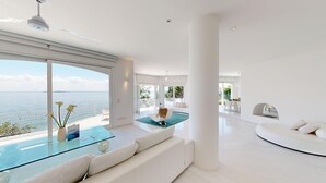 Ein moderner, geräumiger Wohnbereich mit einem großen Glastisch, einem weißen Sofa und Meerblick.