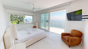 Ein Schlafzimmer mit Bett, Sessel, Fernseher und einem Balkon mit Meerblick.