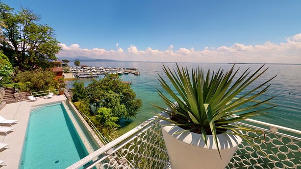 Ein Pool mit Blick auf eine Marina und Boote, umgeben von Grünflächen und wolkenlosem Himmel.