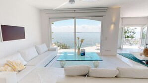 Ein modernes Wohnzimmer mit einem Glastisch, weißen Sofas und Blick auf das Meer.