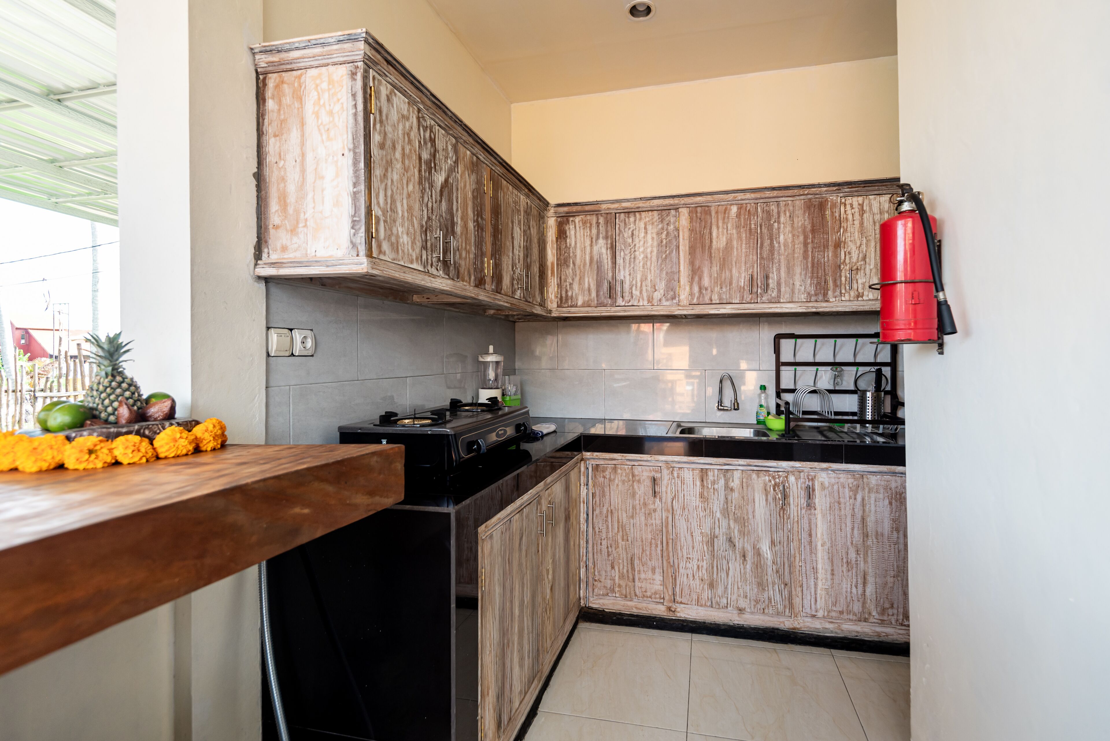 Une cuisine avec des meubles de rangement en bois, une cuisinière noire et un extincteur rouge.
