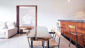 A modern room with a glass dining table, wooden chairs, a sofa, and a bed with white linens.