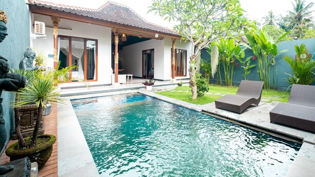 A poolside area with a house, outdoor furniture, and tropical plants.