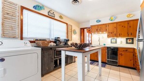 A kitchen with wooden cabinets, a white refrigerator, a washing machine, and a dining table. - Family Tides | Pet-Friendly East Beach Cottage Near Gould's Inlet on St. Simons Island (Saint Simons Island)