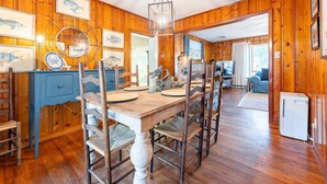 A wooden-paneled room with a dining table and chairs, a blue cabinet, and framed fish artwork on the walls. - Family Tides | Pet-Friendly East Beach Cottage Near Gould's Inlet on St. Simons Island (Saint Simons Island)