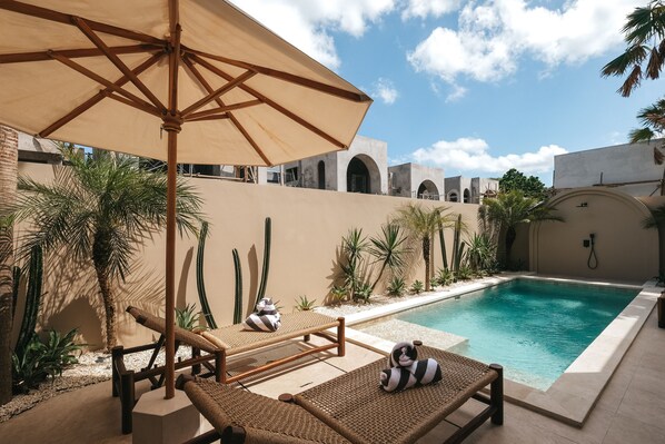 A poolside area with lounge chairs and an umbrella, surrounded by cacti and palm trees. - Limón & Cello Villa (Canggu)