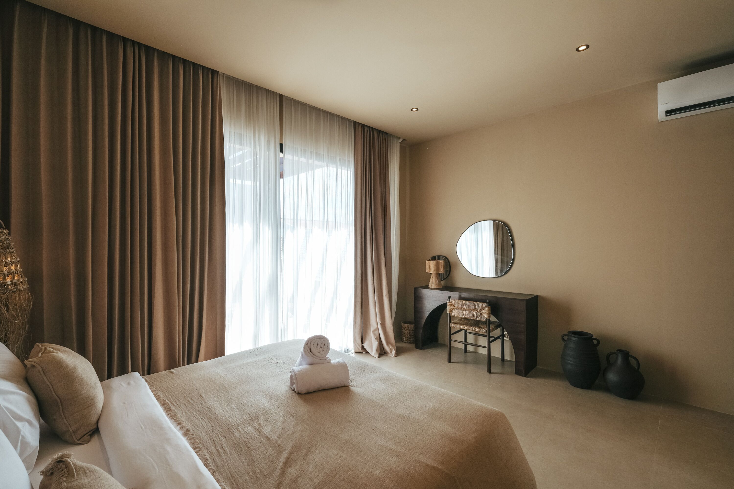 A hotel room with a large bed, a desk with a chair, a mirror, and two vases.