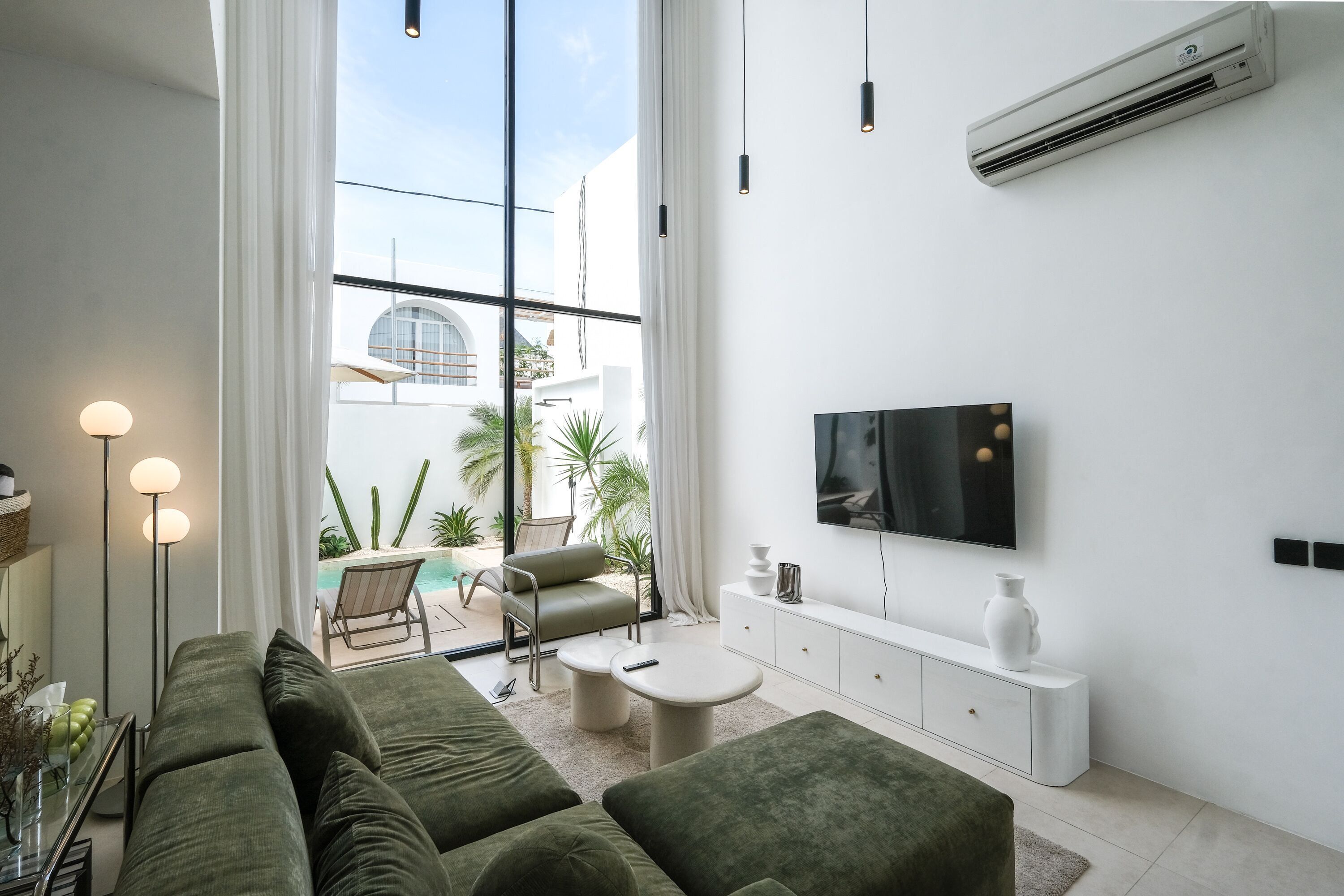 Ein modernes Wohnzimmer mit großem Fenster, Flachbildfernseher, einer Couch, einem Couchtisch und einer weißen Kommode.