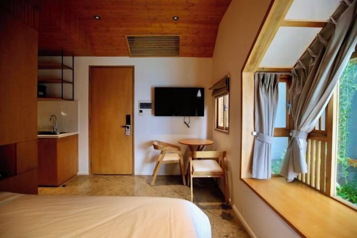 A bedroom with a bed, a desk, a chair, a television, and a window with curtains.