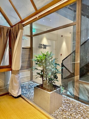 A reception area with a glass partition, a reception desk, a potted plant, and a staircase with a metal railing. - CityHouse VIBE Abora (Ho Chi Minh City)