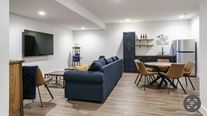 Ett modernt vardagsrum med en soffa, ett matbord och stolar. Det finns också ett köksområde med skåp och ett kylskåp.