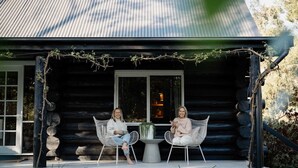Two people seated at a table on a porch with a log cabin background.