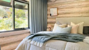 A bedroom with a large window, wooden walls, a bed with striped bedding, and a bedside lamp.