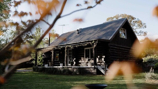 A rustic log cabin with a porch, a chimney, and a small garden area.