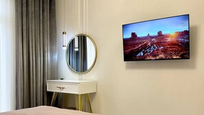 A bedroom with a bed, a bedside table, a mirror, and a wall-mounted TV displaying a landscape scene.