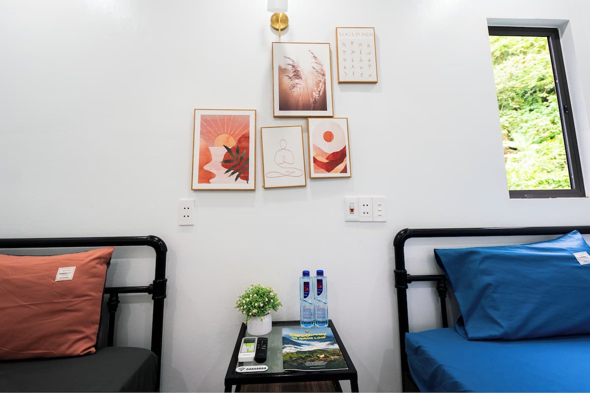 A room with two beds, a small table with a plant and water bottles, and wall-mounted artwork.