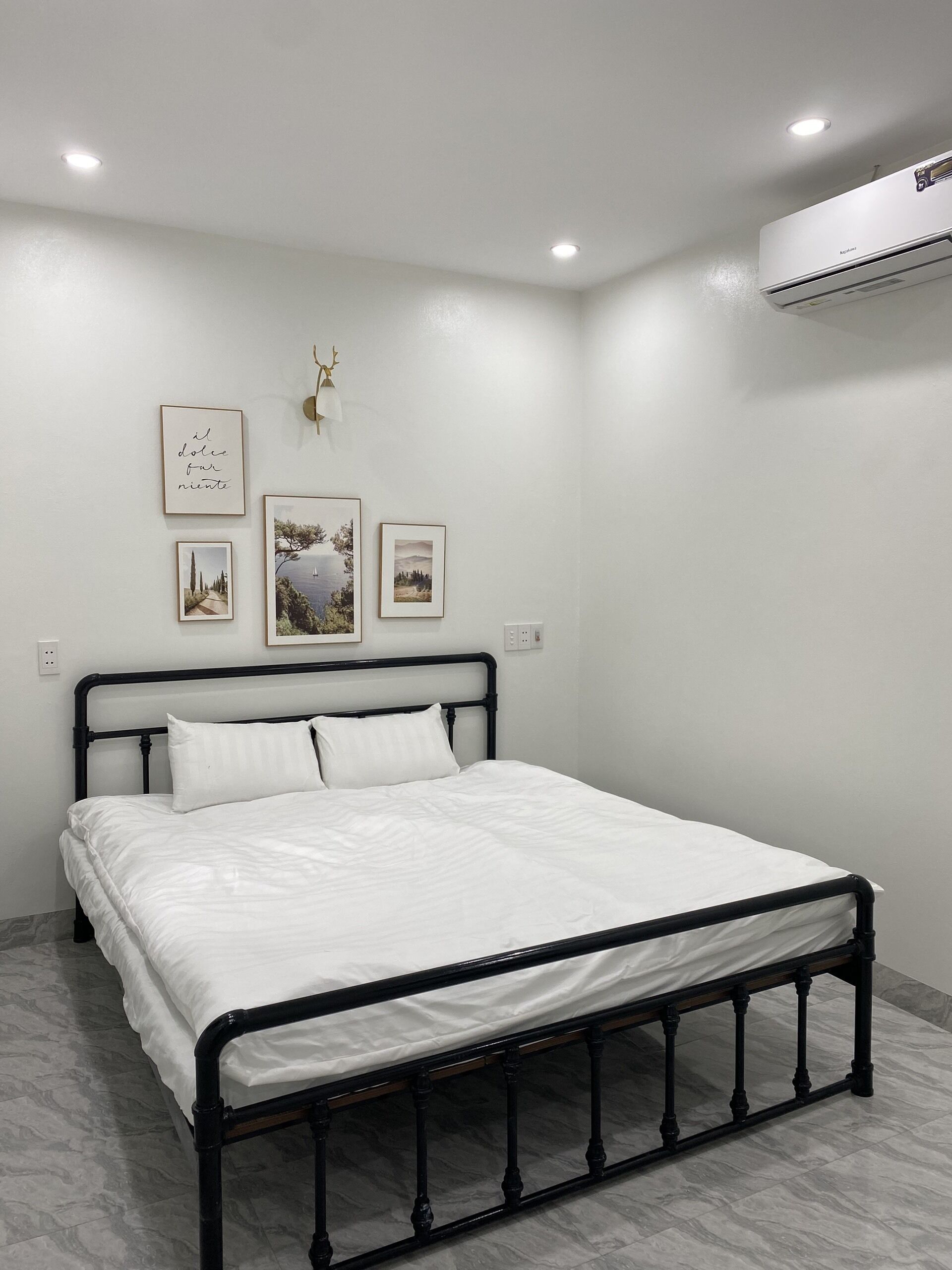 A bedroom with a bed, white walls, and a ceiling-mounted air conditioner.