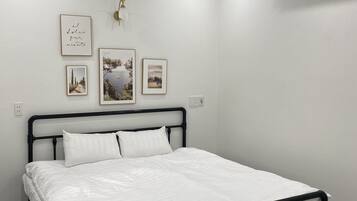 A bedroom with a bed, white walls, and a ceiling-mounted air conditioner.