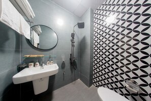 Un baño con lavamanos blanco, un espejo, una ducha y un revestimiento de pared estampado.