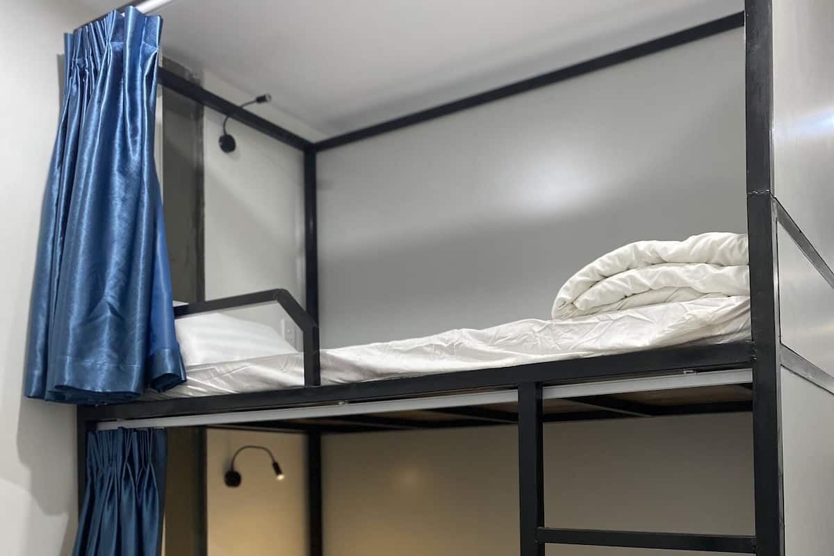 A bunk bed with a blue curtain, white bedding, and a wall-mounted light.